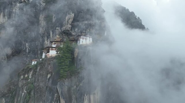 Aerial view of the Taktsang (Tiger's Nest) monastery clinging to the cliffside, shrouded in ethereal mist, Taktsang, Paro, Bhutan.