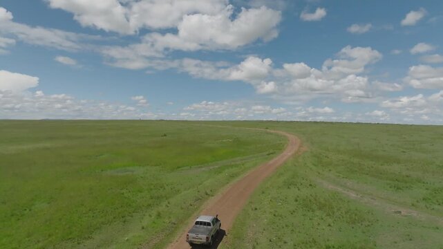 Aerial view of a long path running through a vibrant green field under a partly cloudy sky, Narok, Narok, Kenya.