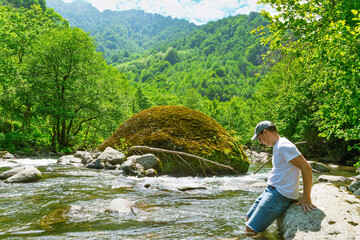 Man sitting by river near moss covered boulder in green valley. Georgia © bykot