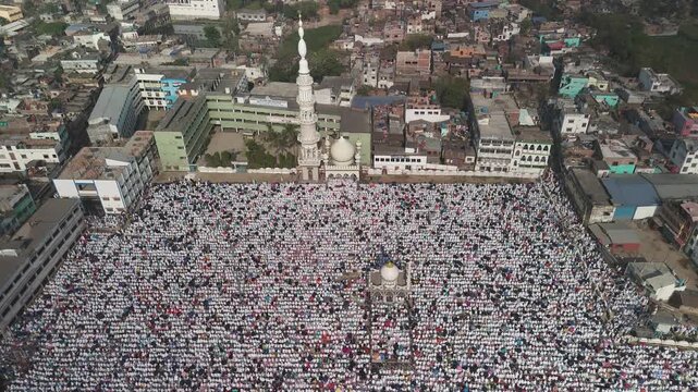 Aerial view of a large religious congregation with white clothing around a mosque with a tall minaret, Malda, West Bengal, India.