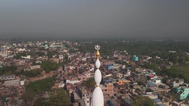 Aerial view of the tall white minaret of a mosque contrasting with the dense urban sprawl and distant green horizon, Malda, West Bengal, India.