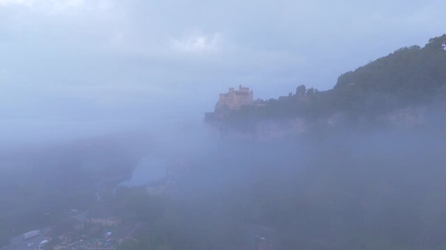 Beynac-et-Cazenac, France - 12 September 2025: Aerial view of Chateau de Beynac perched atop a cliff, overlooking a river shrouded in ethereal morning mist.