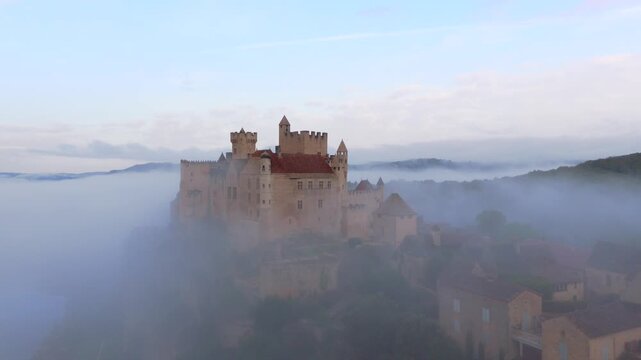 Beynac-et-Cazenac, France - 12 September 2025: Aerial view of Beynac Castle shrouded in thick fog, creating an ethereal and dreamlike scene.