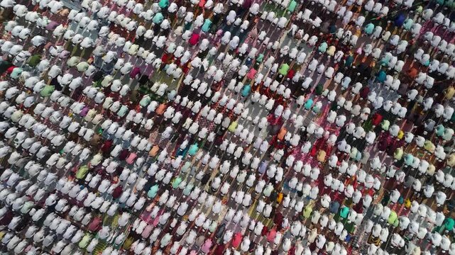 Aerial view of many people praying together, their white clothes contrasting with the colorful mats on the ground, Malda, West Bengal, India.