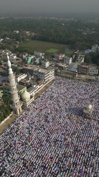 Aerial view of a mosque surrounded by a vast gathering of people, creating a sea of white against the urban landscape, Malda, West Bengal, India.
