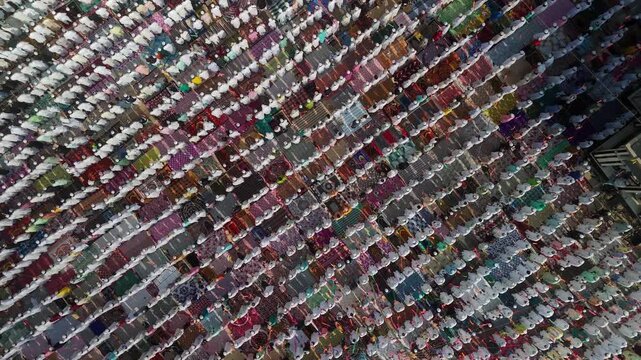Aerial view of a multitude of people praying in neat rows, their colorful mats creating a vibrant tapestry near a mosque, Malda, West Bengal, India.