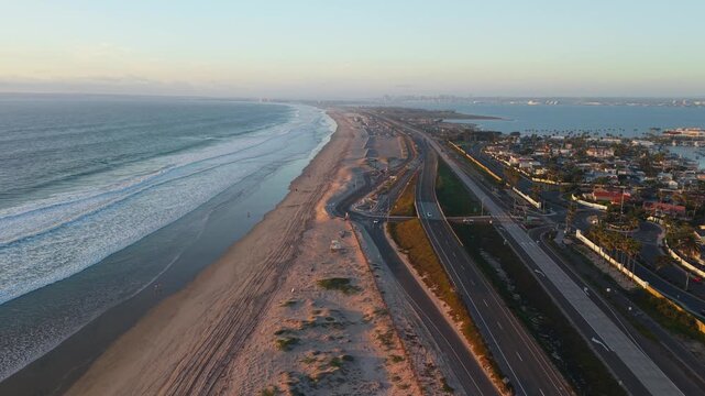 Aerial view of the golden beach meeting the turquoise sea beside a busy highway, the scene bathed in the soft light of dawn, Coronado, California, United States.