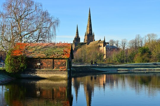 Lichfield Cathedral reflected behind rustic lakeside cottage at sunrise