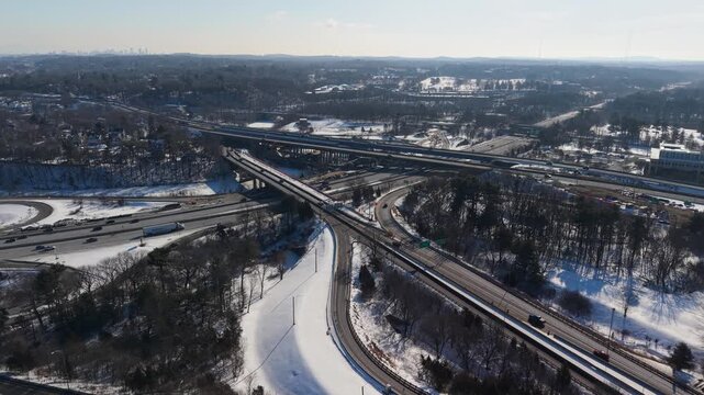 Aerial view of Interstate 95 cutting through a snowy landscape with sparse trees and buildings, the dark asphalt contrasting with the white snow, Salisbury, Massachusetts, United States.