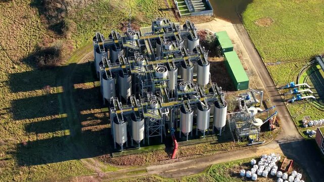 Aerial view of an industrial complex with tanks and metal structures casting shadows on the ground, surrounded by grass, Luton, England, United Kingdom.