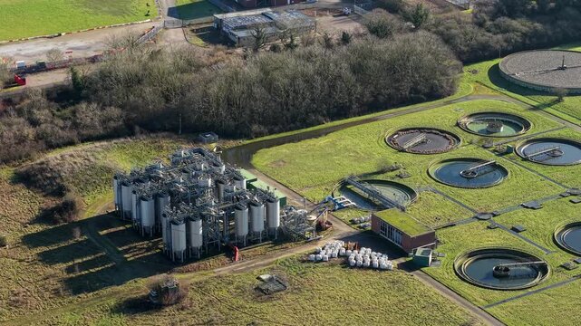 Aerial view of a water treatment plant featuring tanks and circular water pools, set against a backdrop of lush greenery, Luton, England, United Kingdom.