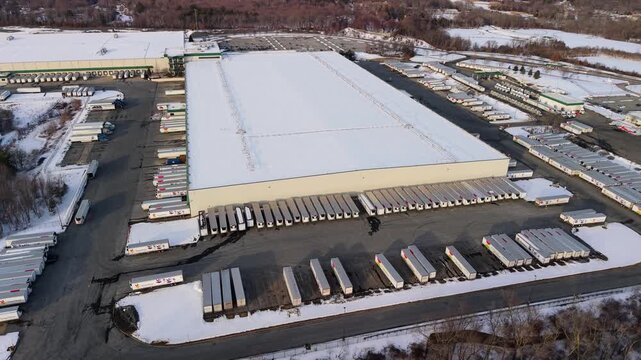 Aerial view of a vast snow-covered warehouse surrounded by rows of trucks, creating a stark contrast against the winter landscape, Fall River, Massachusetts, United States.