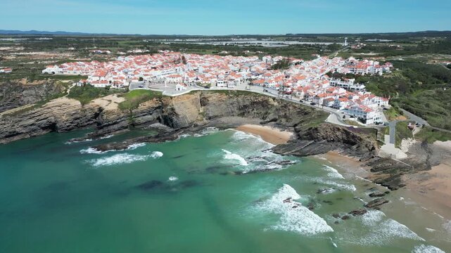 Aerial view of the beautiful coastlines of Zambujeira do Mar, with white buildings and red roofs contrasting with the turquoise waters, Zambujeira do Mar, Beja District, Portugal.