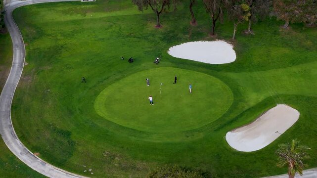 Aerial view of lush green golf course, dotted with sand bunkers and golfers, under a soft light, creating a serene and picturesque scene, San Diego, California, United States.