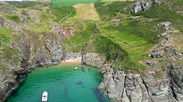 Aerial view of boats in a cove with turquoise water surrounded by cliffs with green grass and a small beach, UK, England, United Kingdom.