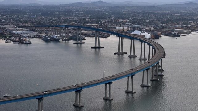 Aerial view of the Coronado Bridge stretching across water, contrasting with the cityscape and industrial docks, Coronado, California, United States.
