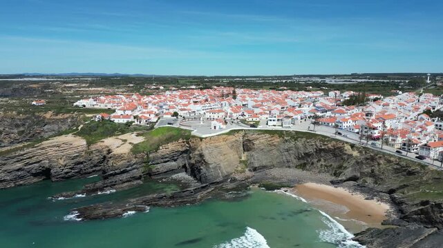 Aerial view of the village with red roofs meeting the blue sea, creating a striking contrast along the rugged coastline, Zambujeira do Mar, Beja District, Portugal.
