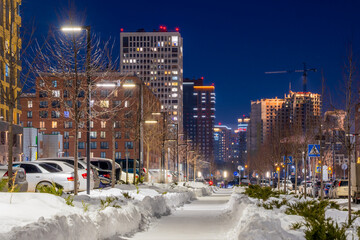 Evening cityscape. Winter view of a snow-covered street in a modern residential area of ​​a large city. Novosibirsk, Novosibirsk Oblast, Siberia, Russia.