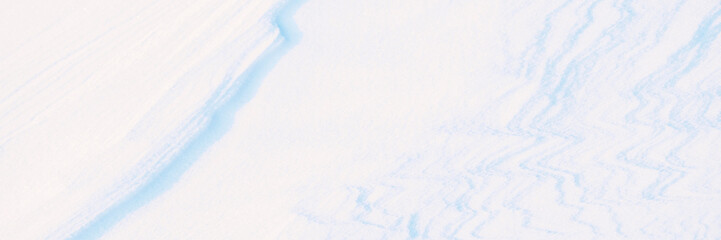 Wide panoramic winter background with snowy ground. Natural snow texture. Wind sculpted patterns on snow surface. Closeup top view with copy space.