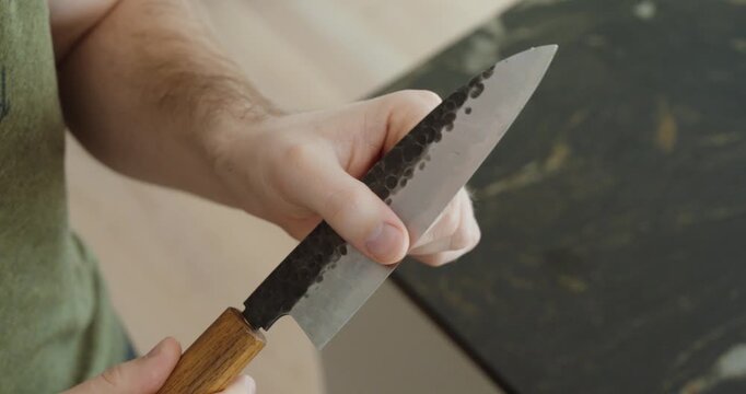 Close-up of hands holding a sharp kitchen knife with a wooden handle, highlighting cooking preparation, blade craftsmanship, and kitchen safety.