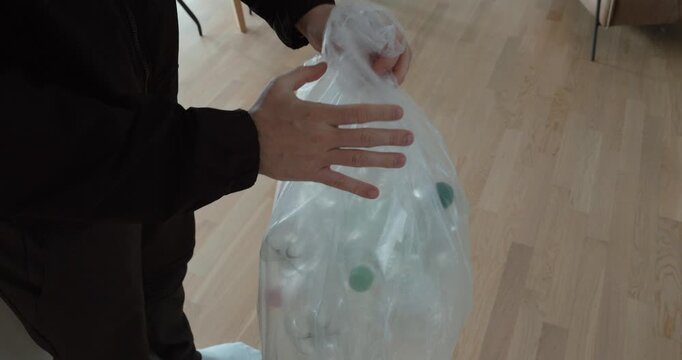 Person tying and lifting a transparent bag filled with empty plastic bottles, symbolizing responsible waste disposal, deposit return systems, and sustainable everyday behavior.