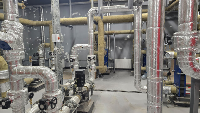 Industrial piping system featuring various insulated pipes, valves, and control panels arranged in mechanical room, showcasing clean and organized layout with metallic surfaces and functional design