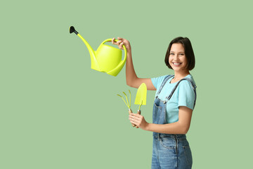 Beautiful young woman with watering can, rake and shovel on green background