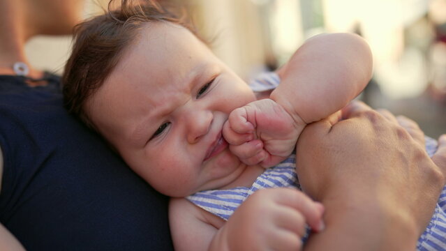 Baby awake stretching body while lying on mother&rsquo;s lap outdoors, hands reaching upward, relaxed and secure, family bonding moment in urban environment during daytime