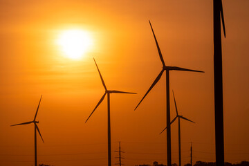 Fototapeta premium Silhouette of an industrial wind turbine farm generating renewable energy against a vibrant sunset sky as a clean technology. distribution of energy,Powerplant,energy transmission,high voltage supply.