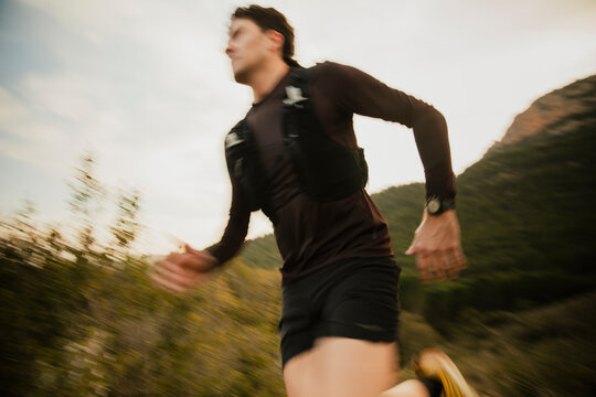 Dynamic motion blur photograph of a trail runner sprinting along a mountain trail during outdoor endurance training. Speed and action captured in natural landscape.