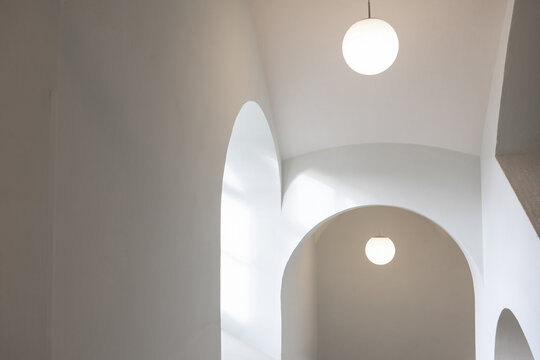 Minimalistische Innenarchitektur mit B&ouml;gen und runden Deckenleuchten in hellem Raum.