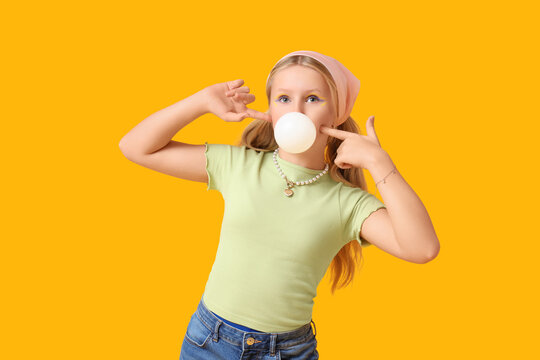 Cute trendy girl blowing bubble gum on yellow background