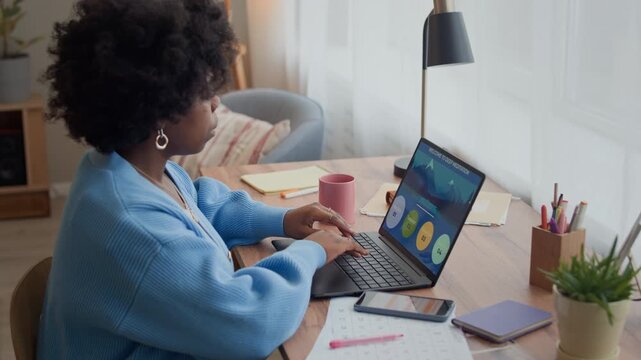 Side view of young African American lady setting meditation application on wireless laptop while sitting at table with calendar and smartphone