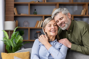 Senior couple embracing and smiling in their living room, representing enduring love, happiness,...