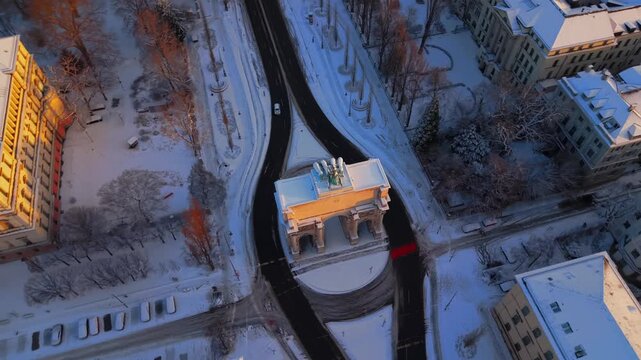 Flugaufnahme Muenchen sunrise over Siegestor Victory Gate in Germany. Golden hour drone footage of the snow covered Triumphbogen Triumphal Arch and Friedensmahnmal Peace Memorial in Munich city.