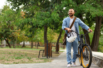 Young happy man with helmet and bicycle walking in park