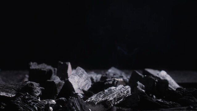 Low key close up of charcoal chunks in a grill with faint smoke on dark background, ideal for BBQ, heat, fuel and industrial texture concepts.