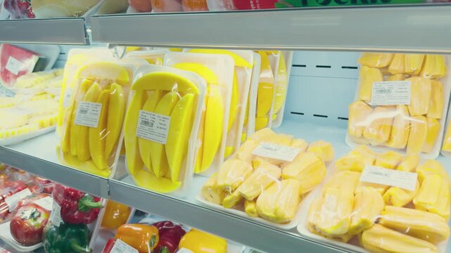 Pre cut tropical fruits including peeled mango and jackfruit, alongside fresh bell peppers, packaged for convenience and displayed in a cooled grocery store refrigerator for customer selection