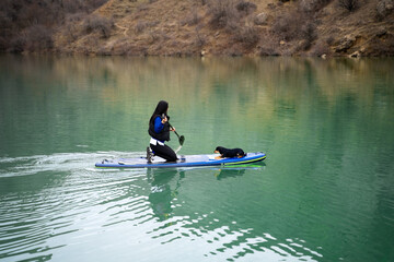 Woman on sup board with her dog on peaceful lake in daylight. Female paddleboarding with pet in nature, enjoying surfing on SUP board with domestic pet in nature.Active healthy lifestyle.