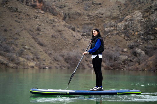 Sde view of woman on sup board on scenic mountain lake in spring. Peaceful young female enjoying her paddleboarding adventure in nature. Active tourism, healthy lifestyle.

