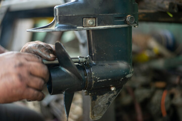  hands of a master auto mechanic repair a gasoline outboard marine engine. The mechanic's hands are stained with oil and salidol. In the frame is the propeller and pump of the boat unit © Rystemys