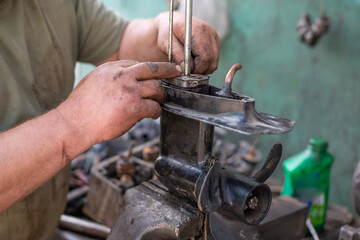 The hands of a master auto mechanic repair transmission of outboard marine engine. The mechanic's hands are stained with oil and salidol. In the frame is the propeller and pump of the boat unit © Rystemys