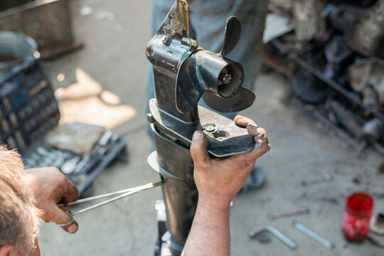 The hands of a master auto mechanic repair a gasoline outboard marine engine. The mechanic's hands are stained with oil and salidol. In the frame is the propeller and pump of the boat unit