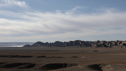Vast Desert Landscape with Rugged Mountain Range under Cloudy Sky, Natural Scenery for Travel or Environmental Themes