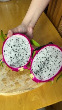 Hands slicing a fresh, vibrant pink dragon fruit on a light wooden cutting board, preparing the healthy tropical pitaya with a sharp knife for culinary use