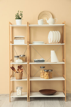 Shelf unit with kitchen utensils and food near beige wall in room