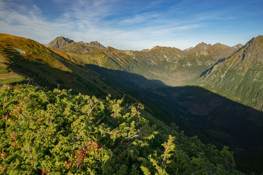 View of deep shadows stretch across the valley floor contrasting with the sunlit mountain ridges and green vegetation in Liptovske Kopy, Presov Region, Slovakia.