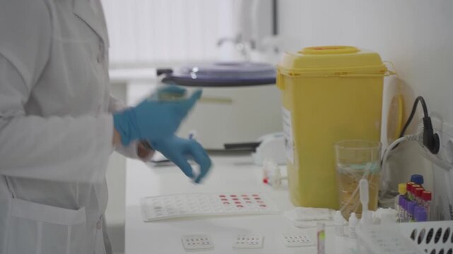Laborant in blue gloves conducts blood group testing using reagents and test plates. Clinical specialist uses automatic pipette and test tubes for hematology analysis in a modern medical laboratory