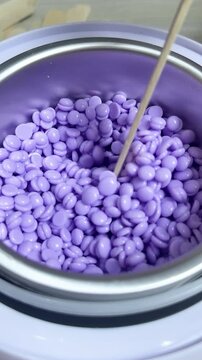 Purple wax beads filling a personal warmer, ready to melt for professional looking hair removal at home or salon, close up overhead view of hard wax pellets in container