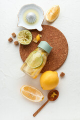 Bottle of infused water with lemon and juicer on light background